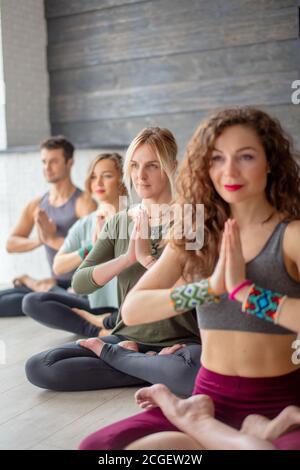 Beautiful woman with long curly hair practicing Yoga Exercise in fitness centre, sitting in lotus posture over training people background Stock Photo