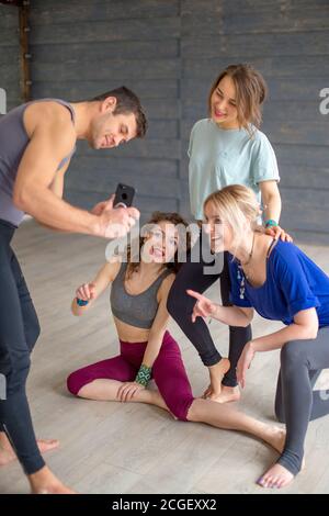 Athletic man in sportswear showing photos from social media profile via smartphone to his group female mates from yoga class after a workout Stock Photo