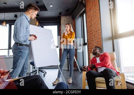 Young dynamic multiracial business team male and female coworkers discussing around a flip chart white board in meeting room Stock Photo