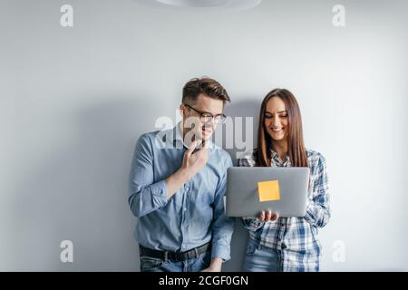 Two caucasian heterosexual architects collegues discussing project of new skyscraper building using laptop, standing against white office wall Stock Photo
