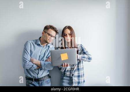 Two heterosexual architects collegues discussing project of new contemporary skyscraper using laptop, standing against white office wall Stock Photo
