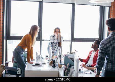 Two caucasian designers females sharing new ideas about project to his partners in office working room. Multiethnic coworkers discussing over new busi Stock Photo
