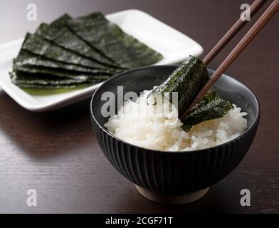 Rice in a teacup set against a wooden backdrop and wrapped with chopsticks in seaweed. Breakfast in Japan Stock Photo