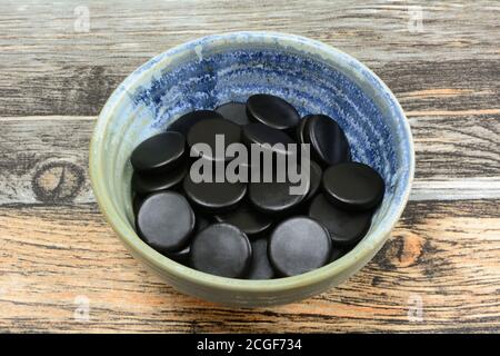Round black licorice candies in small ceramic snack bowl on table Stock Photo