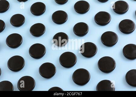 Black licorice candy coins in rows on light blue background Stock Photo