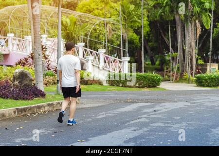 Back view portrait of a Asian man in fitness wear walking and jogging for good health in public park. Jogger in nature. Man enjoying Peaceful nature. Stock Photo