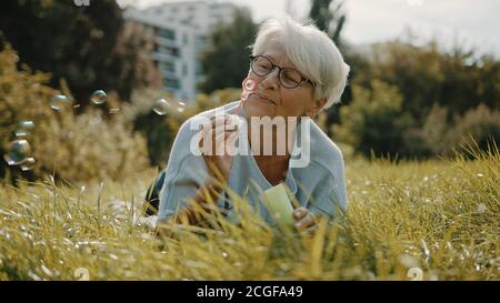 Retired senior woman enjoying freedom. Childish grandma blowing soap bubbles in the park. High quality photo Stock Photo