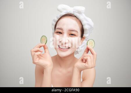 Young woman with clay facial mask holding cucumber slices isolated on white background Stock Photo