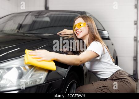 Car wash service, worker beautiful girl polishes and clean microfiber headlights on black auto Stock Photo