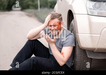 Car accident, man sits with bloodied head near wheel, screaming and crying Stock Photo