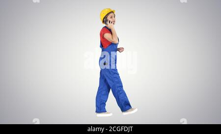 Young female architect consultant talking on phone while walking on gradient background. Stock Photo