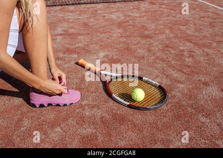 Female legs in pink sneakers, Tying shoelaces in sunlight. Female Athlete starting tennis workout on outdoot court. Stock Photo
