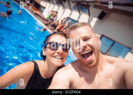 Cheerful happy couple guy and woman make selfie photo in hotel pool, summer vacation travel Stock Photo