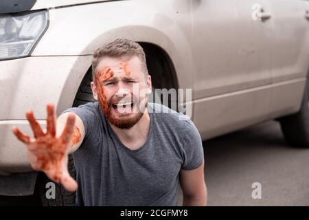 Car accident, man sits with bloodied head near wheel, screaming and crying Stock Photo