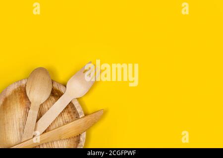 Wooden cutlery on a wooden plate and on a yellow background Stock Photo
