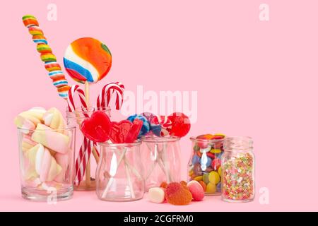 Assorted candies and lollipops in crystal jars on a pink background Stock Photo