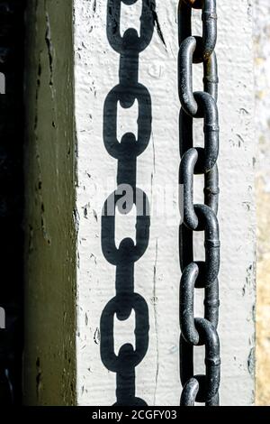 A thick metal chain hanging from a gate post whre it has been left after a security padlock has been undone. Stock Photo