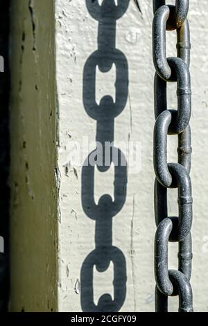 A thick metal chain hanging from a gate post whre it has been left after a security padlock has been undone. Stock Photo