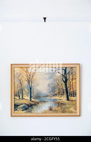 A simple picture of a forest hanging in it's frame on white painted wall. Stock Photo
