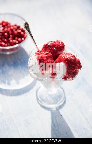 Cream bowl with three balls of ice cream and cranberry jam, berries in a transparent plate, long shadows from the dishes . Close up. Vertical orientat Stock Photo