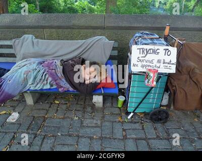 A HOMELESS MAN LYING ON A BENCH WHILE SLEEPING NEAR CENTRAL PARK Stock Photo