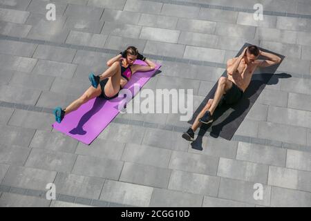 Young couple in sports outfit doing morning workout outdoors. Man and woman doing cardio and strenght exercises, practicing activity for lower and upper body. Sport, healthy lifestyle concept. Stock Photo