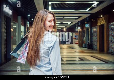 Beautiful young brown-haired girl with long hair with a lot of packages on the shoulder in a mall. Cheerful, happy shopping girl Stock Photo
