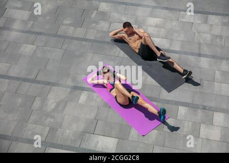 Action. Young couple in sports outfit doing morning workout outdoors. Man and woman doing cardio and strenght exercises, practicing activity for lower and upper body. Sport, healthy lifestyle concept. Stock Photo