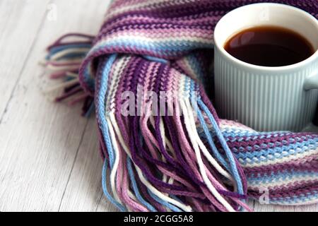 Blue cup of hot tea is wrapped in a warm striped multi-colored scarf. Autumn background with copy space Stock Photo