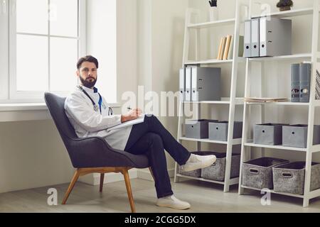 Man doctor therapist looking at camera, listening to patient and making notes in medical clinic Stock Photo