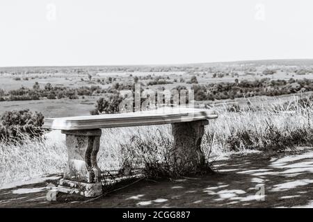 Marble white bench in trees shadow with view on river valley in distance from hill. Black and white. Zmiyevsky cliffs on Siverskyi Donets River in Ukr Stock Photo