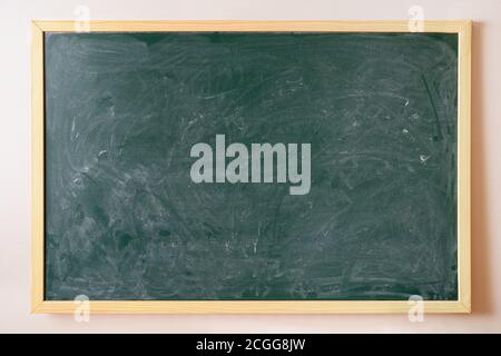 Green chalk dirty college blackboard with wooden frame hanging on the wall Stock Photo