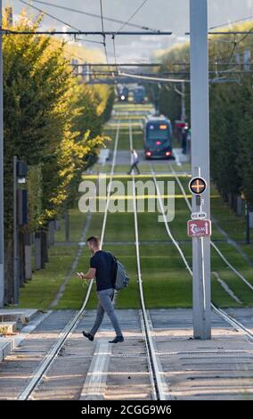 Bordeaux, France - 27th September, 2018: Man using phone crossing the tracks at Stalingrad tram stop during morning  rush hour in the city of Bordeaux Stock Photo
