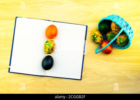 Easter eggs lying in the blue basket and on a yellow wooden table, a book for notes as a copy of pastes and eggs lying on it Stock Photo