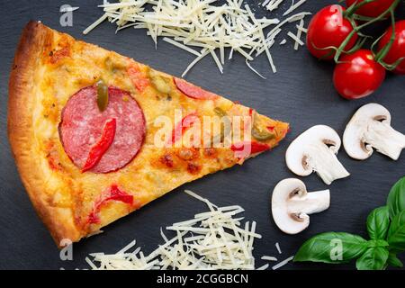 Tasty hot pizza with ingredients and pizza cutting knife on a black texture background. Top view Stock Photo