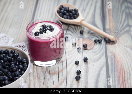 On a wooden background is a glass with a diet drink blueberry smoothie with whipped cream and a plate of blueberries on a lace napkin, there is a wood Stock Photo
