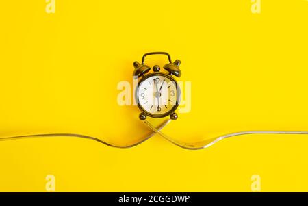 Black clock on a yellow background. Alarm clock on two forks, trend concept time .