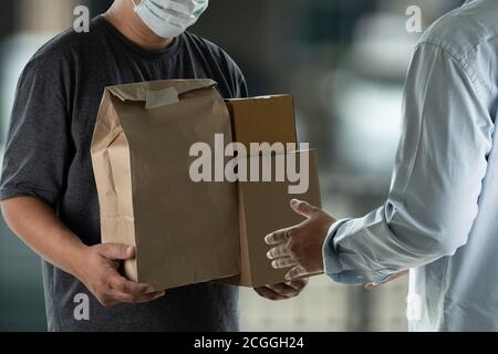 Delivery man holding cardboard boxes and accepting delivery man in protective mask Stock Photo