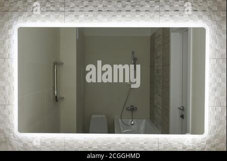 Wide big mirror in bathroom with illumination on tile background Stock Photo