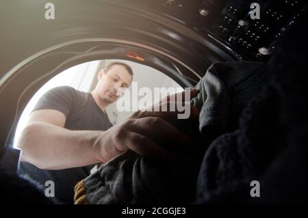 Young man loading cloth in open door of washing machine wide view Stock Photo