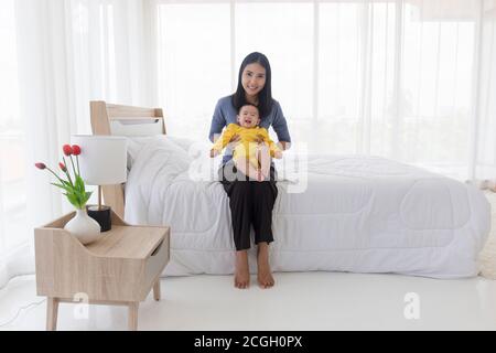 An Asian mom is happily playing with her baby in bed. Stock Photo