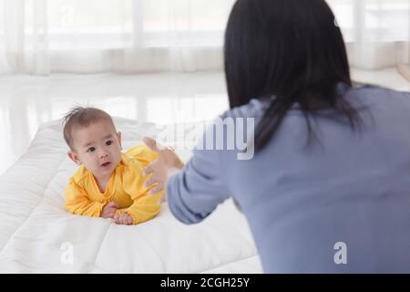 An Asian infant who is practicing crawling With her mother sitting on the other side of her soft white cloth in the bedroom Stock Photo