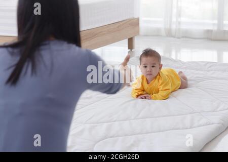 An Asian infant who is practicing crawling With her mother sitting on the other side of her soft white cloth in the bedroom Stock Photo