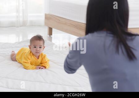 An Asian infant who is practicing crawling With her mother sitting on the other side of her soft white cloth in the bedroom Stock Photo