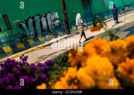 A Mexican woman walks in front of piles of marigold flowers (Flor de muertos) during the Day of the Dead celebrations in Oaxaca, Mexico. Stock Photo