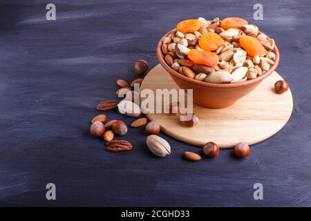 Mixed different kinds of nuts in ceramic bowl on black wooden background with copy space. hazelnut, brazil nut, almond, pumpkin seeds, cashew. Stock Photo