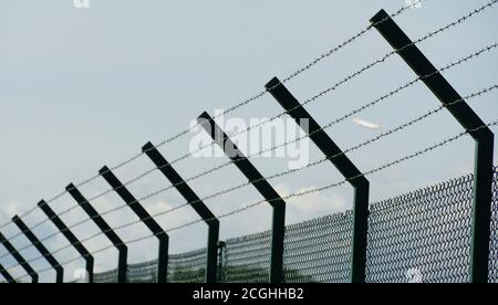 A tall fence around the ground of Zurich Airport made of woven wire and enhanced with barbed wire as protection from unauthorized entry. Stock Photo
