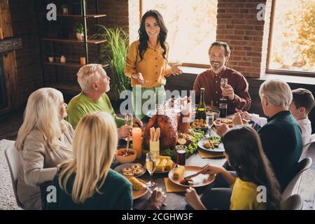 Portrait of nice attractive cheerful family friends friendship parents meeting eating festal luncheon turkey drinking champagne mom saying toast at Stock Photo