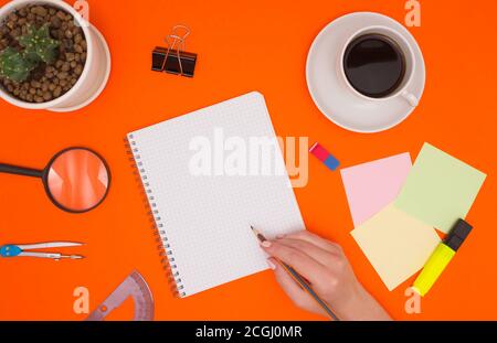 The concept of working in an office, mockup in a notebook. The hand holds a pencil and is about to write in an empty notebook. Stationery, coffee, and Stock Photo