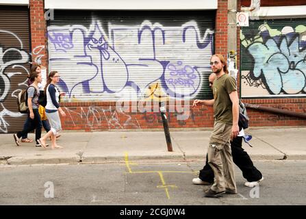 Young people walking on the street past a wall of graffiti in the Kensington-Market neighbourhood of downtown Toronto, Ontario, Canada. Stock Photo